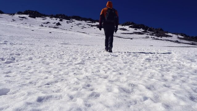 Low angle: Lone hiker walks on snow toward distant mtn summit ridge
