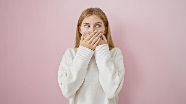 Beautiful blonde girl, standing in shock over mistake, covers mouth with hands on isolated pink background