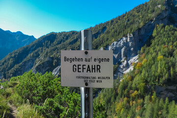Obraz premium Information sign with scenic view of ountain ridges in Hochschwab massif, Styria, Austria. Board says: Attention. Danger. Enter at your own risk. Idyllic hiking trail in summer