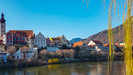Scenic view of idyllic colourful houses next to river Mur in Frohnleiten in Styria (Steiermark), Austria. Tourism in alpine town in summer. Tree branch hanging in foreground. Travel destination - obrazy, fototapety, plakaty
