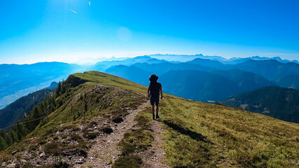 Man with baby carrier on hiking trail with scenic view of magical mountain peaks Karawanks and Julian Alps seen from Goldeck, Latschur group, Gailtal Alps, Carintha, Austria. Austrian Alps in summer