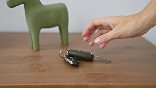A person's hand placing car keys near a green ceramic horse on a wooden table indoors.