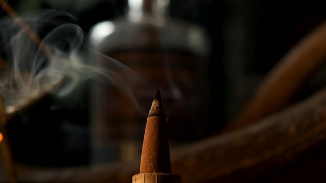 Close up of a incense cone burning with smoke spreading in a dark esoteric setting, in slow motion