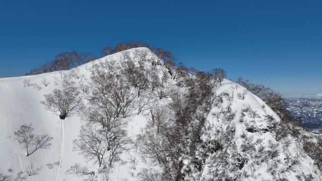 Aerial wide establishing orbiting ascending shot of Japan's mount myōkō summit peak, on a clear winter day, a volcanic mountain in Myoko-Togakushi Renzan National Park region