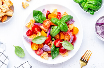 Italian salad with tomatoes, stale bread, red onion, olive oil, salt and green basil, white table background, top view