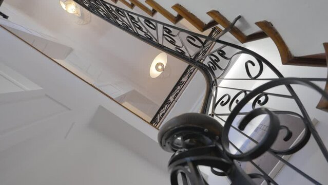 Stairwell in slow motion, with its wrought iron banister and its white walls with moldings, the steps are made of wood