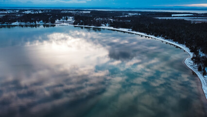 Sun and clouds reflecting on lake in winter with snowy shoreline