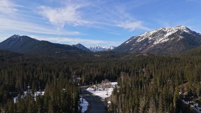 Backwards scenic shot of snow capped mountain range with river above evergreen forest in Cle Elum in Washington State.
