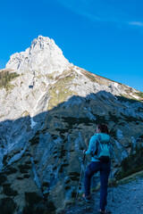Fototapeta premium Hiker woman with panoramic view of majestic mountain peak Foelzstein in untamed Hochschwab mountain region, Styria, Austria. Scenic hiking trail on in remote Austrian Alps. Wanderlust in alpine summer