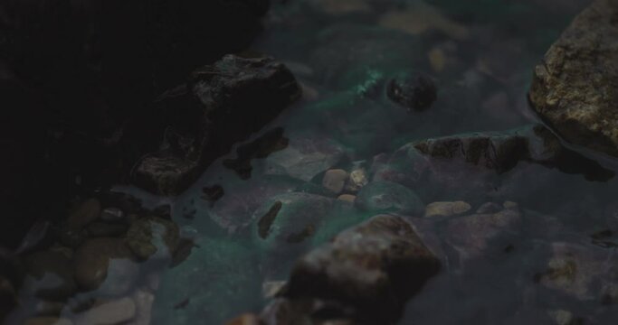 Closeup of grey and brown tan pebbles rocks with jagged edges as clear water fills around