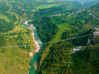 Aerial view of a Tibetan suspended bridge in Nepal is a primitive type of bridge in which the deck lies on two parallel load-bearing cables that are anchored at either end. Wild nature - 777643183