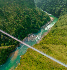 Aerial view of a Tibetan suspended bridge in Nepal is a primitive type of bridge in which the deck lies on two parallel load-bearing cables that are anchored at either end. Wild nature - 777643334