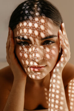 Young woman with hands by face under speckled shadow light effect
