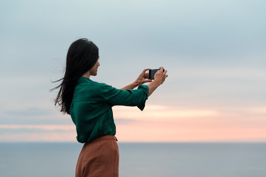 Happy woman taking pictures with phone at sunset
