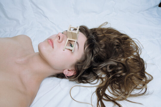 Young woman lying on white blanket. Miniature chair on her face.  