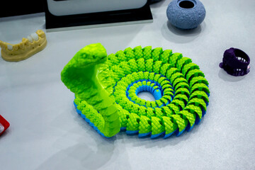 Green snake toy model printed on a 3D printer from melted plastic. Snake-shaped object created by 3D printer. Detailed green prototype printed on 3D printer close-up. New modern additive technologies