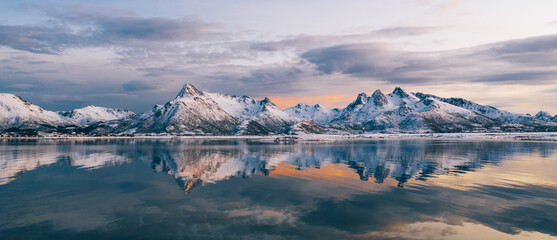 Breathtaking bird's eye view of high mountain rocky peaks covered with white snow reflected in Norway sea water. Breathtaking panoramic fjords landscape of Lofoten in winter, calm beauty of nature