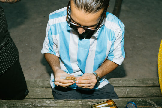 Man in soccer shirt rolling a joint