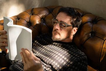 mature man reading a book on sofa 