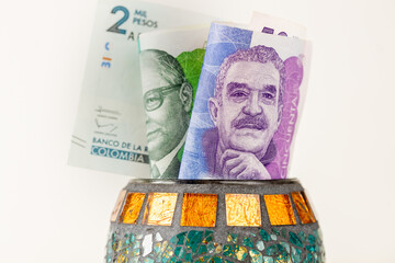 Colombian money, 50 and 100 pesos banknotes sticking out from a decorative bowl, Financial concept, Saving and economics - 777649155