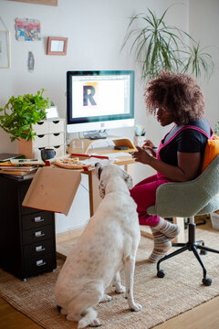 Pregnant designer woman eating pizza in home office warning her dog