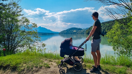 Man with baby carriage on idyllic hiking trail along Drava river. Scenic view of mountain peaks of...