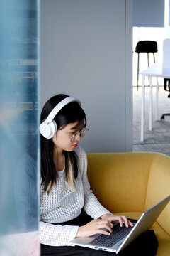 Young office worker wearing headset and using laptop on sofa