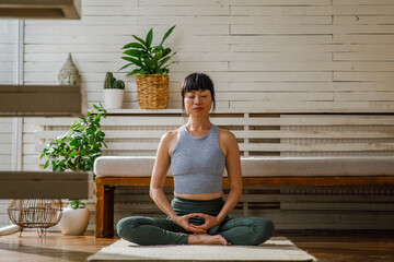 Asian woman meditating calmly on yoga mat at home