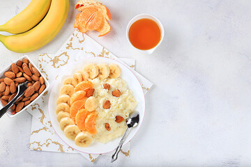 Healthy breakfast with ingredients, flat lay, rice pudding with bananas, honey, tangerines and almonds on a sunny table. Healthy and natural nutrition concept, lifestyle, nutrition for children