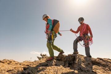 Two people are climbing a mountain together. One of them is wearing a backpack. The other person is...