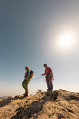 Two people are standing on a rocky hillside, one of them holding a leash. The sun is shining brightly, creating a warm and inviting atmosphere. Concept of adventure and outdoor exploration