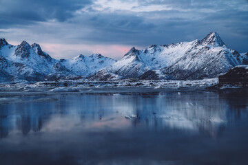 Sea covered with ice surrounded by snowy mountains at sundown