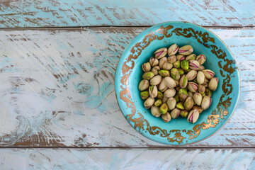 Fototapeta na wymiar A turquoise antique bowl full of pistachios standing on a white wooden textured table, macro closeup shot 