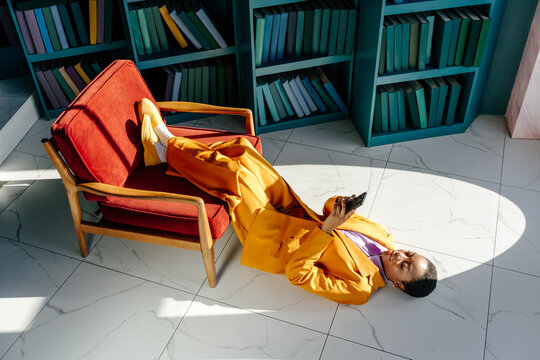 Young black woman lying on floor and using smartphone