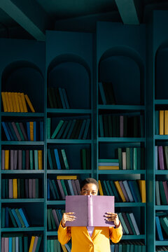 Woman looking out from behind opened book 