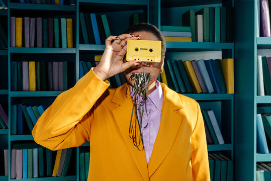 Unrecognizable woman in suit hiding face with cassette