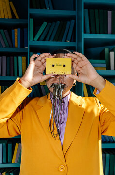 Unrecognizable woman in suit holding cassette and chewing tape