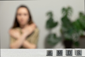 Letters EMDR written on grey stone cubes blocks. Female touching and tapping her shoulders in...
