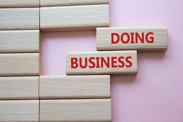 Doing Business symbol. Concept word Doing Business on wooden blocks. Beautiful pink background....