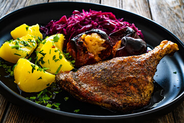 Roast duck thigh with boiled potatoes, apples and red cabbage on wooden table
