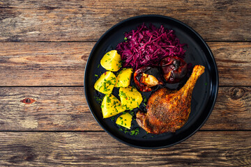 Roast duck thigh with boiled potatoes, apples and red cabbage on wooden table
