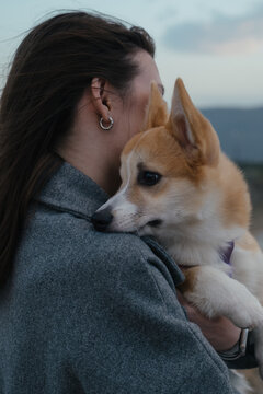 Woman holding Welsh Corgi dog while standing against blue sky