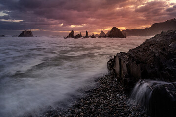 warm sunrise on the beach of Gueirua, Asturias with a dramatic sky and the high tide partially...