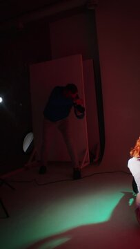 Photographer capturing a sitting woman with red hair under colored lighting. Studio photography session with creative lighting for artistic design.