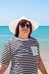 An elderly woman in a white hat on the seashore. Summer holiday on the coast in retirement