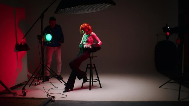 Photographer working with a model in a studio setup with colored gels on lights. Fashion photography shoot with a dynamic pose and red background.