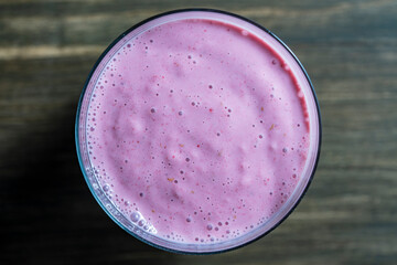 Raspberry banana smoothie in glass on a wooden table, closeup, top view