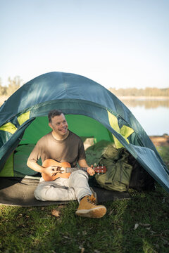 A young man with Down syndrome camping is playing the ukulele