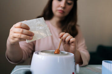 Selective focus shot of female artisan craftperson pouring soy wax into pan to make candles. Process of making handmade natural scented candle. Creative occupation of making trendy diy candles.