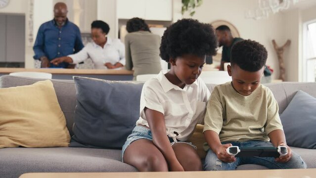 Boy and girl playing handheld computer game at home with multi generation family in background - shot in slow motion